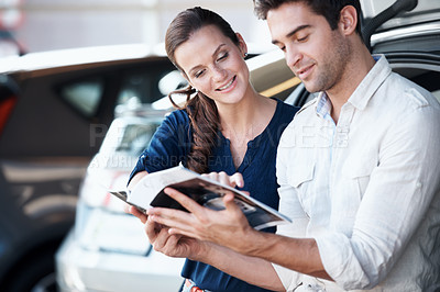 Buy stock photo Couple, choice and happy at car dealership with brochure for purchase, buying and point to deal. Man, woman and smile by trunk for catalog, insurance option or showroom for customer or client