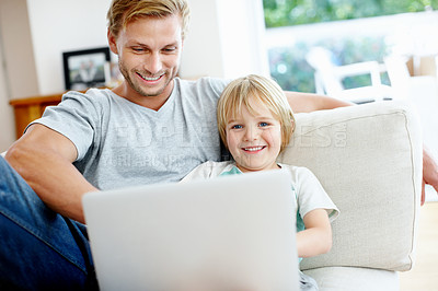 Buy stock photo Cute little boy smiling at you while using a laptop on the couch with his dad