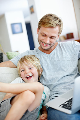 Buy stock photo Cute little boy laughing with his dad while using a laptop on the couch