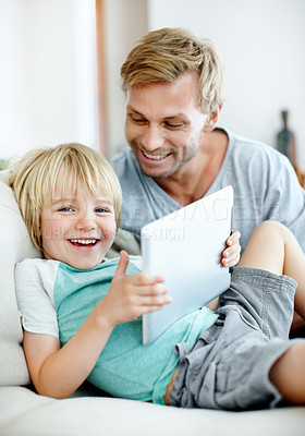 Buy stock photo Cute little boy smiling at you while holding a digital tablet on the couch with his dad