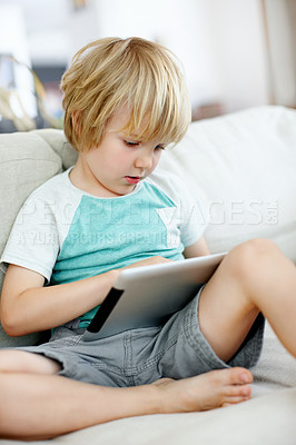Buy stock photo Cute little boy using a digital tablet on the couch at home