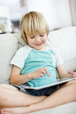 Buy stock photo Cute little boy using a digital tablet on the couch at home