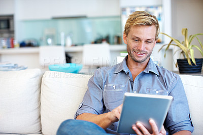 Buy stock photo Handsome young guy using a digital tablet on the sofa at home