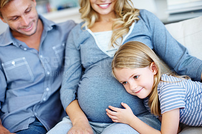 Buy stock photo Cute little girl sitting on the sofa with her father and pregnant mother and listening to her mother's belly