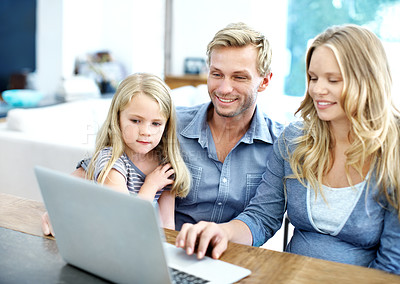 Buy stock photo Cute young family looking at a laptop together while at home
