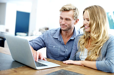 Buy stock photo Cute young couple looking at a laptop together at home