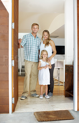 Buy stock photo Young family standing in the doorway of their home with welcoming smiles