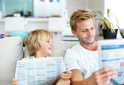 Buy stock photo Cute little boy pretending to read a newspaper like his father while on the sofa at home