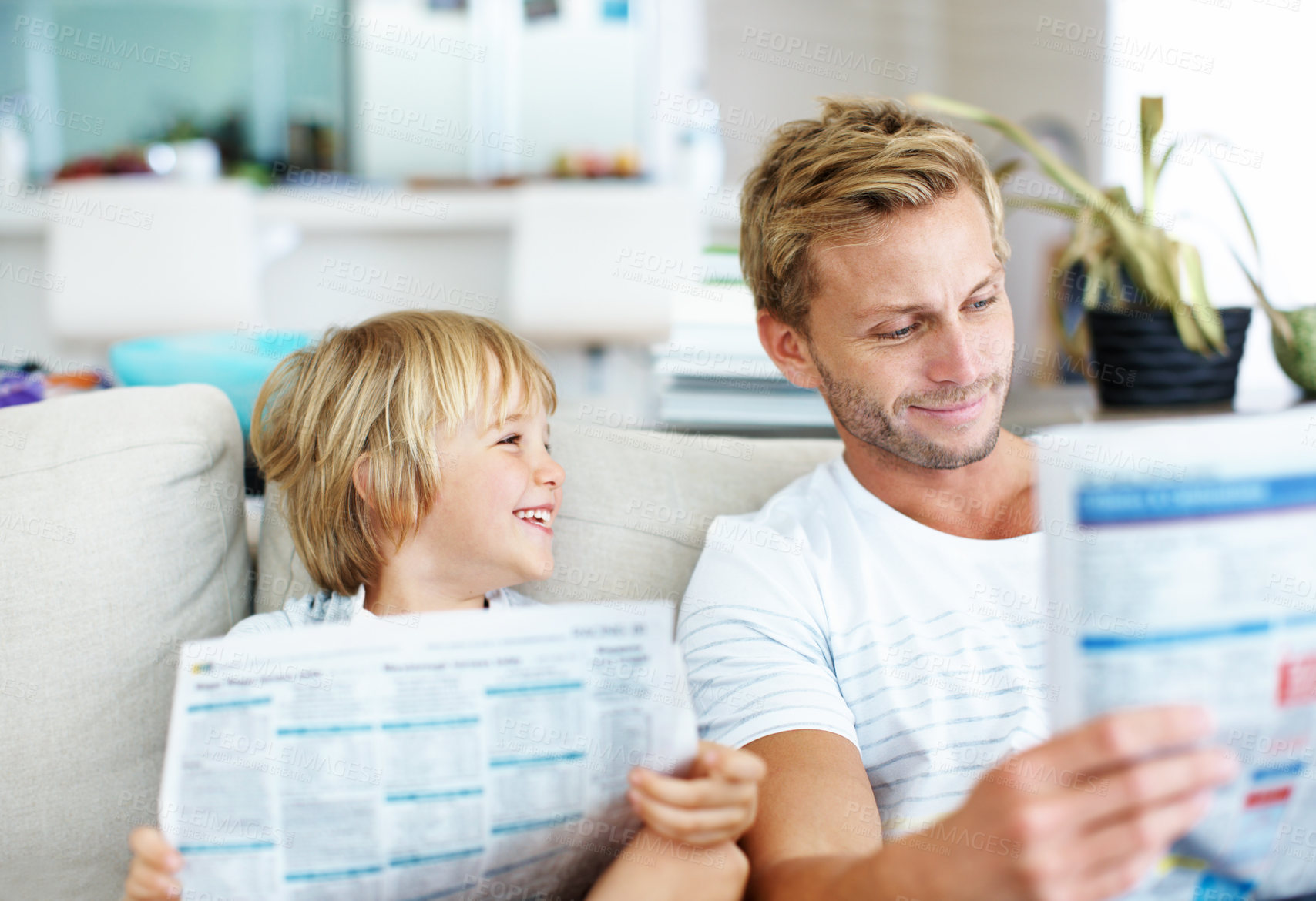 Buy stock photo Smile, newspaper and father with son on sofa in home for bonding, cartoon strip and headline. Relax, support and reading article with man and child in family house for comic or story bulletin