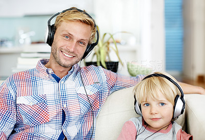 Buy stock photo Cute little boy wearing headphones and listening to music on the sofa with his father
