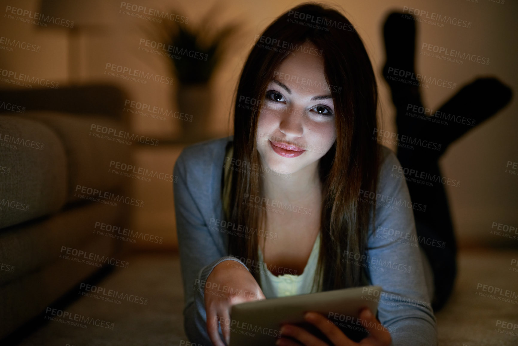 Buy stock photo Portrait of a teenage girl holding a digital tablet while lying on the floor