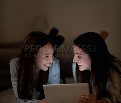 Buy stock photo Two teenagers laughing and holding a digital tablet while lying on the living room floor
