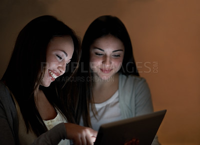 Buy stock photo Two teenage girls browsing on their digital tablet at night