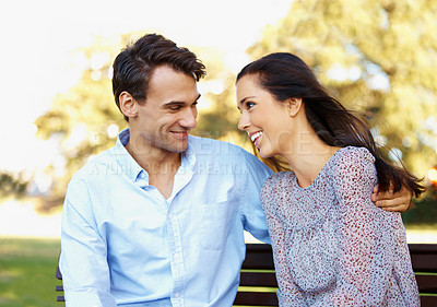 Buy stock photo Loving young couple talking happily on a park bench on a sunny afternoon
