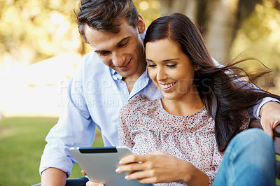 Buy stock photo Happy young couple using their digital tablet outdoors in a park