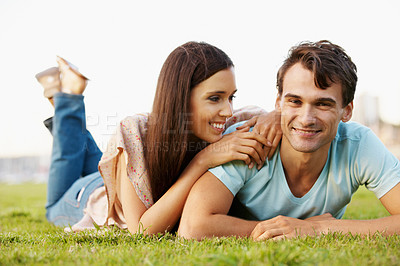 Buy stock photo Happy young couple posing lovingly while lying on some grass in a park