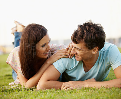 Buy stock photo Loving couple lying on the grass in a park talking 