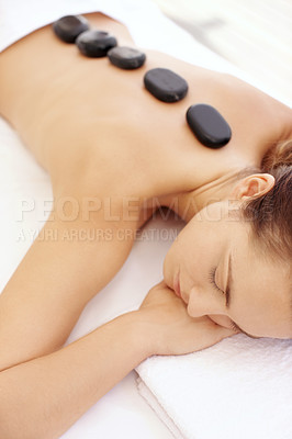 Buy stock photo Beautiful young woman enjoying a hot stone treatment while lying on a spa bed 