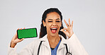 Doctor, phone and green screen or ok sign for approval, positive results or telehealth advertising. Woman, studio portrait and wink by tech as motivation, app review or feedback on white background 