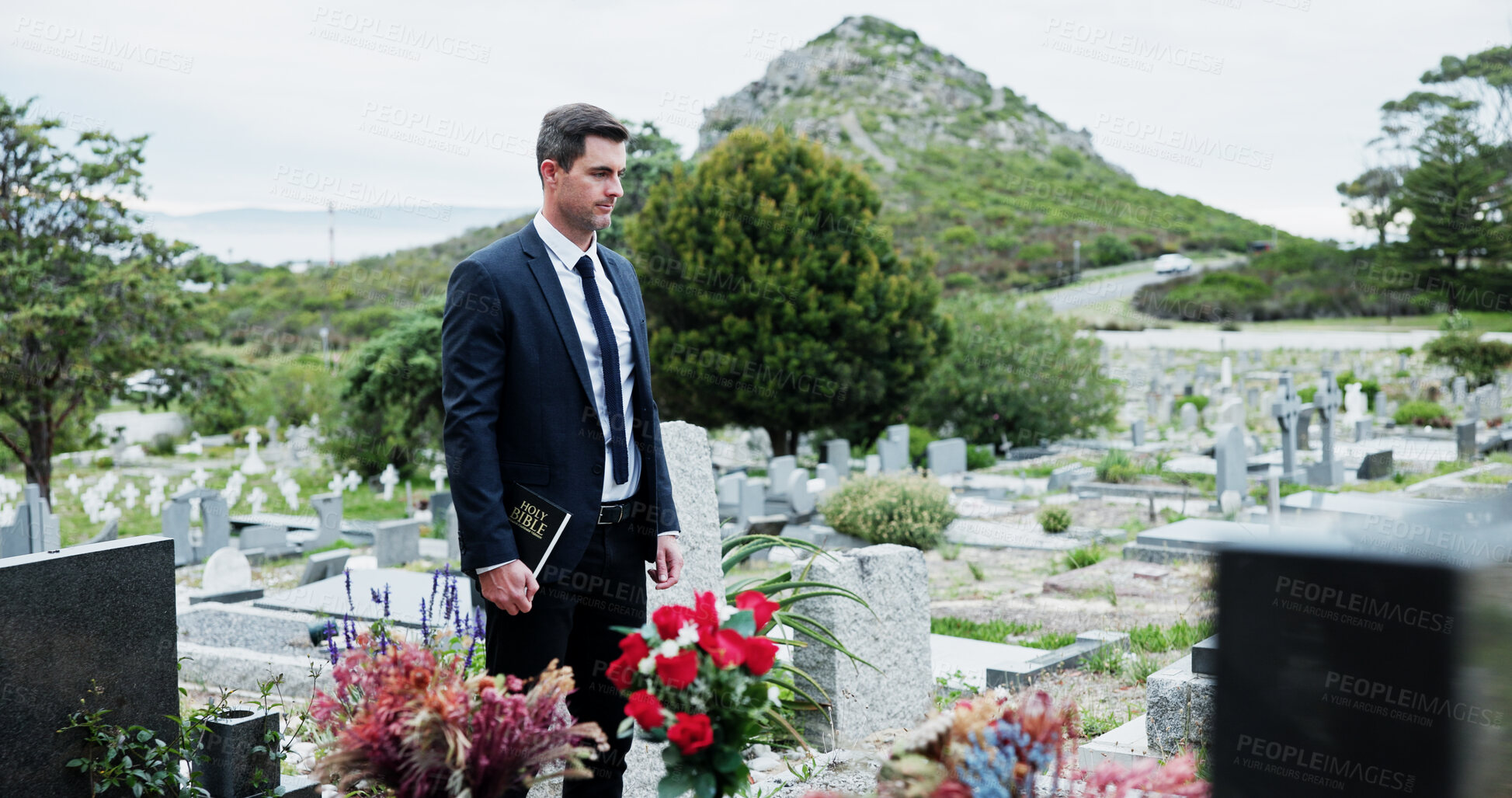 Buy stock photo Sad, man and funeral in graveyard with tombstone, bible and spiritual for burial ceremony of loved one. Christian, person and mourning in cemetery outdoor with gravestone, grief and memorial service.