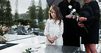 Sad, child and rose in graveyard with tombstone, funeral and people mourning for burial ceremony. Family, girl and flower in cemetery outdoor with grief, sorrow and gravestone for memorial service.