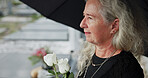 Elderly, woman and umbrella at cemetery with flowers, grieving loved one and thinking about past memory. Sad, old person and reflection at graveyard outdoor with roses, mourning and sorrow for death.
