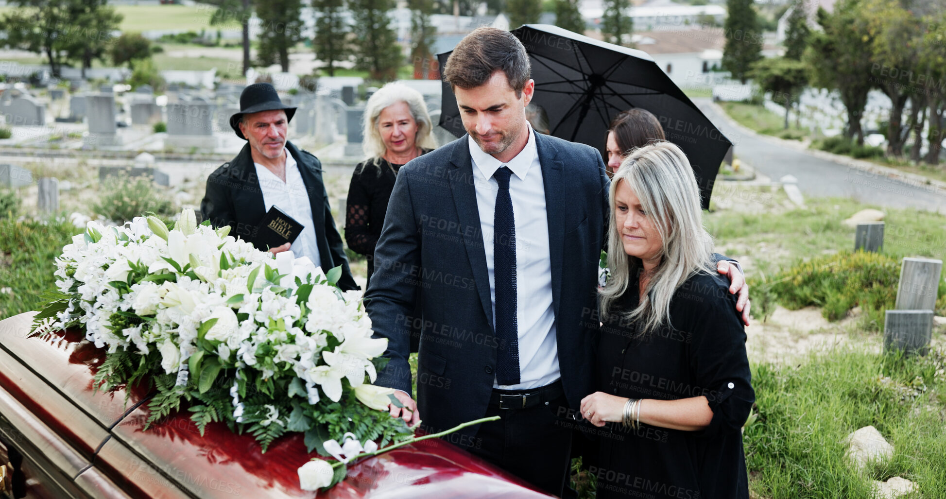 Buy stock photo Casket, comfort and family in cemetery, funeral for memorial service or flower bouquet. People, sad or burial ceremony in graveyard, roses or emotion to grief, loss or greeting with empathy or coffin