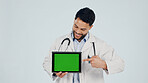 Doctor, pointing or happy man with tablet green screen in studio for Telehealth app or marketing. Male person, healthcare worker or smile with technology display for advertising on a white background