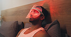 Man, beauty and light with uv mask in bed for facial, skincare or anti aging treatment in home. Relax, male person or red LED cosmetics for skin protection, collagen or blood circulation in bedroom