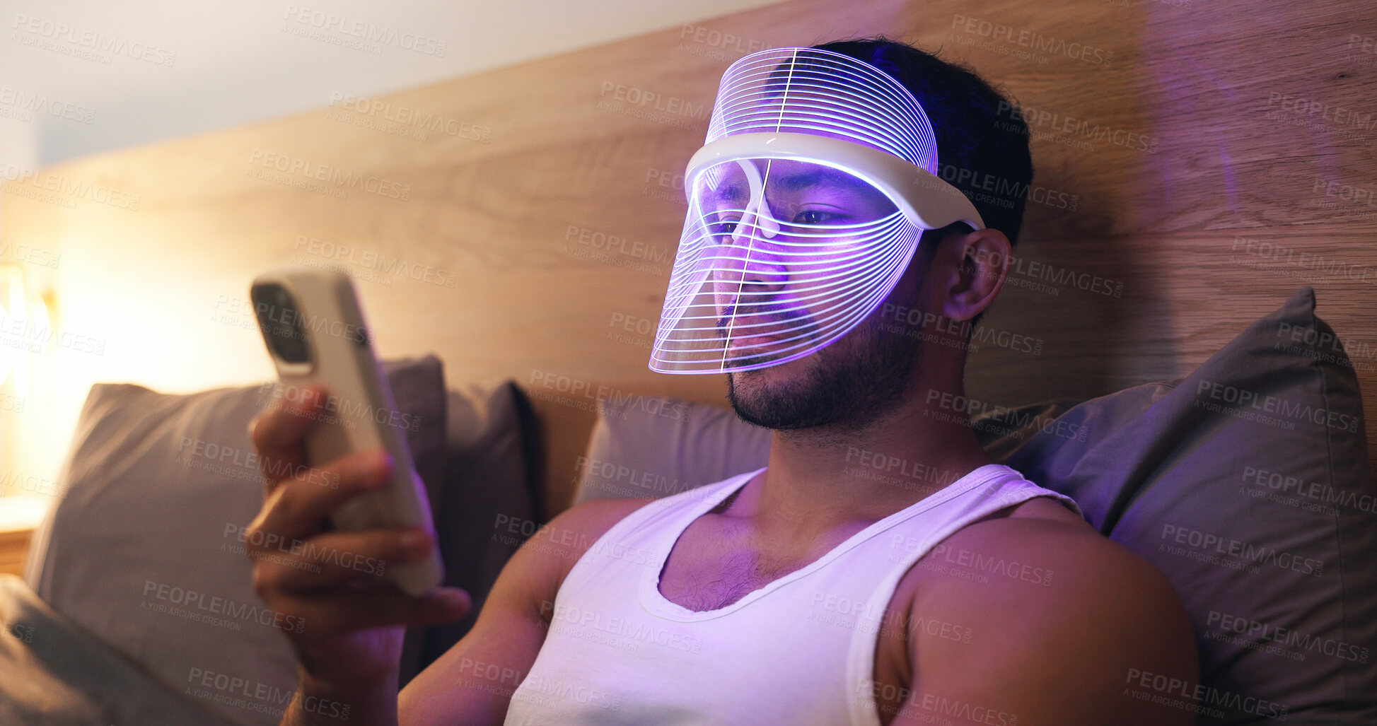 Buy stock photo Phone, bed and man in LED mask, research and browsing website for light therapy benefits. Male person, skincare and cosmetics at house with facial tech, beauty tips and mobile app for acne treatment
