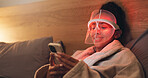 Red light, skincare and woman with phone in bedroom for beauty, wellness and collagen production. Health, relax and person in bed with LED phototherapy tech for dermatology or mask treatment in home