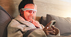 Red light, dermatology and woman with phone in bed for beauty, wellness and collagen production. Health, relax and person in bedroom with LED phototherapy tech for skincare or mask treatment in home