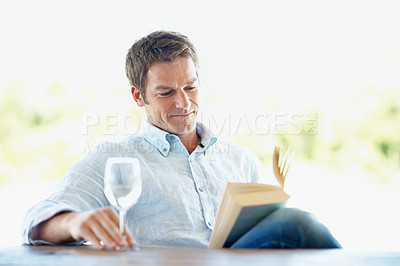 Buy stock photo A content mature man enjoying a glass of wine and reading a good book
