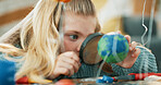 Magnifying glass, science and girl with planet model for project, discovery or assignment. Learning, lens and child with inspection of earth, astronomy or research for school homework in house