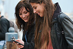 Best friends using smartphone browsing text messages in waterfront two women sharing gossip on social media with mobile phone technology