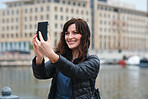 Beautiful travel woman taking selfie photo using smartphone camera in waterfront harbour sharing vacation holding mobile phone
