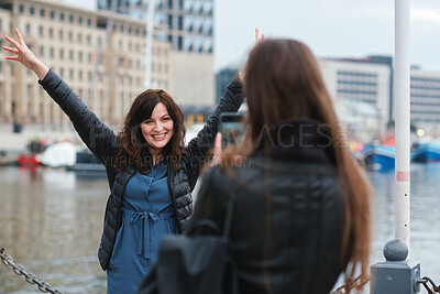 Buy stock photo Friends, phone and photography with picture in city, freedom and social media post on holiday. Smile, woman and mobile at lake harbor for travel, getaway gathering and capture memory on vacation trip