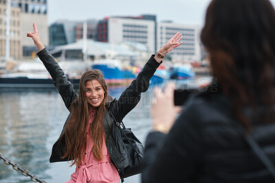 Buy stock photo Travel, picture or friends at harbor with phone, fun hangout or bonding post on weekend break. Happy, digital photo or women in town with arms up, trip connection or memory capture for social media.