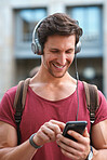 Attractive man using smartphone in city wearing headphones listening to music smiling happy enjoying mobile technology