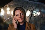Woman using smartphone having phone call talking on mobile phone holding umbrella in rainy city at night