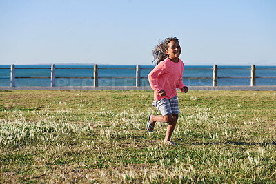 Buy stock photo Freedom, running and smile of child at ocean for break, holiday or vacation excitement. Development, energy and growth with happy girl outdoor on grass lawn for morning summer or weekend getaway