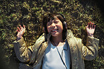 Funny little asian girl wearing headphones lying on grass laughing having fun listening to music in park