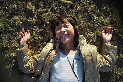 Buy stock photo Top view, headphones and Asian kid on grass with music, smile and listening to radio song on vacation. Above, child and girl with audio on holiday, happiness and streaming sound for relax in nature