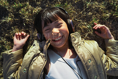 Buy stock photo Above, headphones and Asian kid on grass with music, smile and listening to radio song on vacation. Top view, child and girl with audio on holiday, happiness and streaming sound for relax in nature