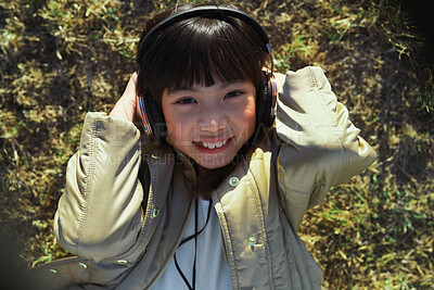 Buy stock photo Above, headphones and Asian kid in nature with music, smile and listening to radio song on vacation. Portrait, adorable child and girl with audio, happiness and streaming sound for relax on grass