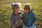 Happy children playing in park little boy and girl having fun brother and sister sitting on grass at sunset