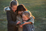 Happy little girls using smartphone playing game on mobile phone in park at sunset