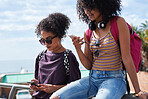 Twin sisters using smartphones in city relaxing on summer day browsing social media texting on mobile phones