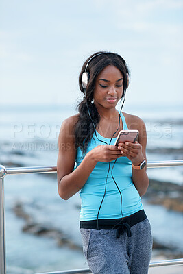 Buy stock photo Woman, headphones and fitness by beach with phone, exercise break and listen to music from mobile app. Active, black person or runner outdoor by ocean with promenade, wellness or audio tech for radio
