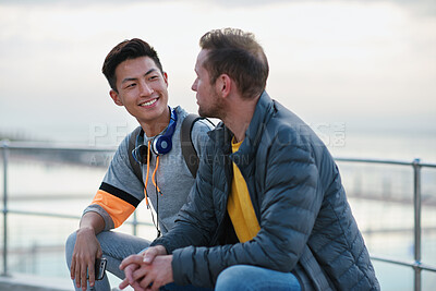 Buy stock photo Men, friends and chat on promenade at beach with smile, bonding and conversation on seaside vacation. People, relax and holiday with discussion, memory or tourism with break on getaway by ocean